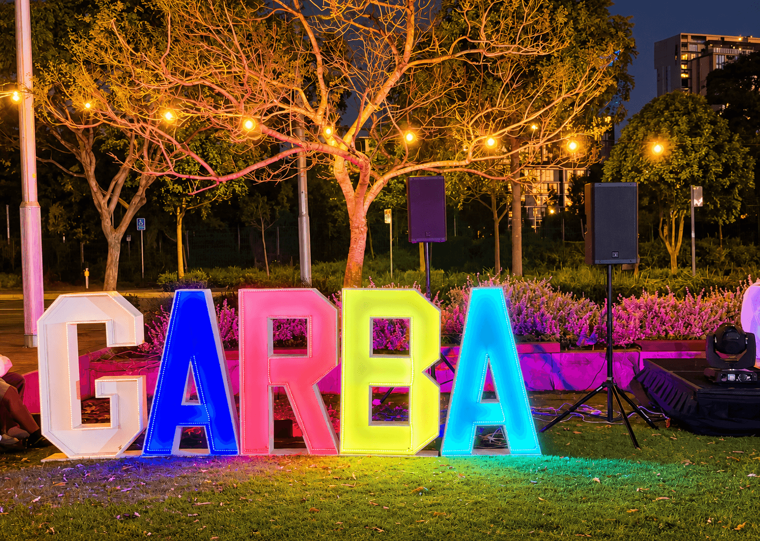 Illuminated GARBA letters beneath warm decorative tree lights